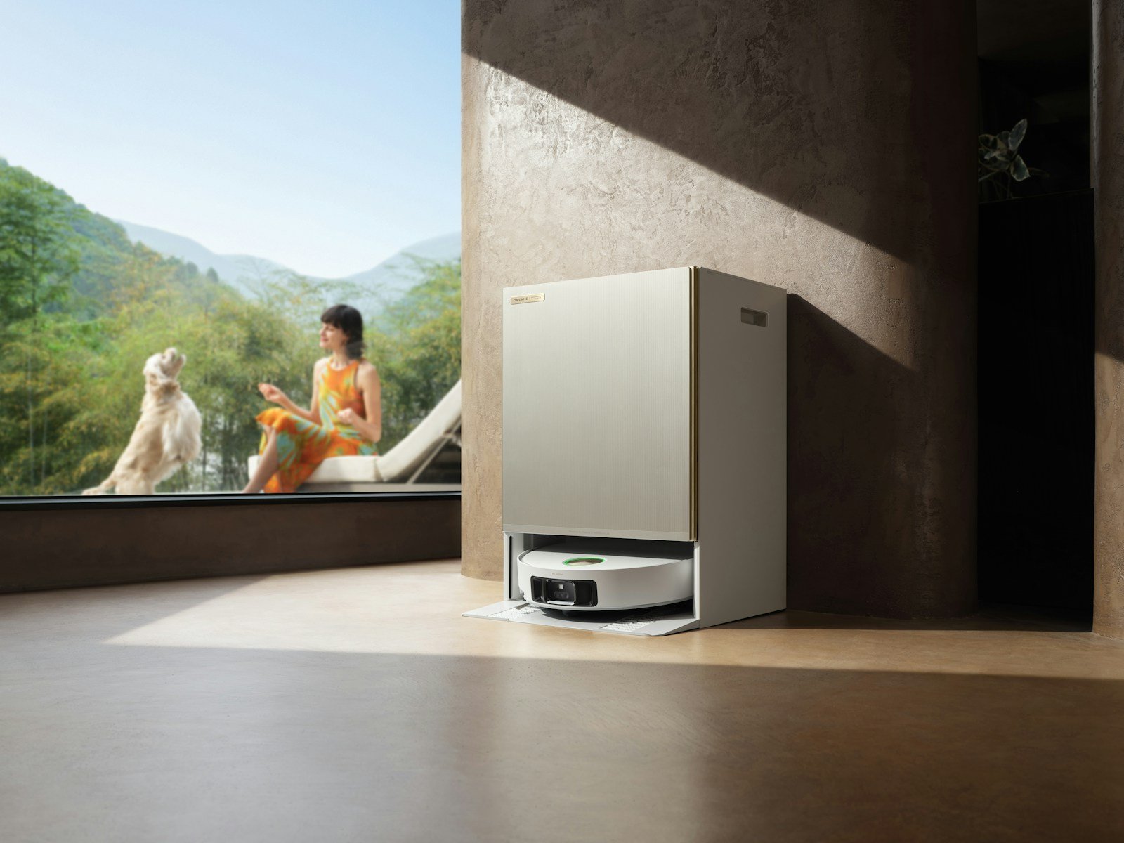 Woman and dog relax by large window with robot vacuum.